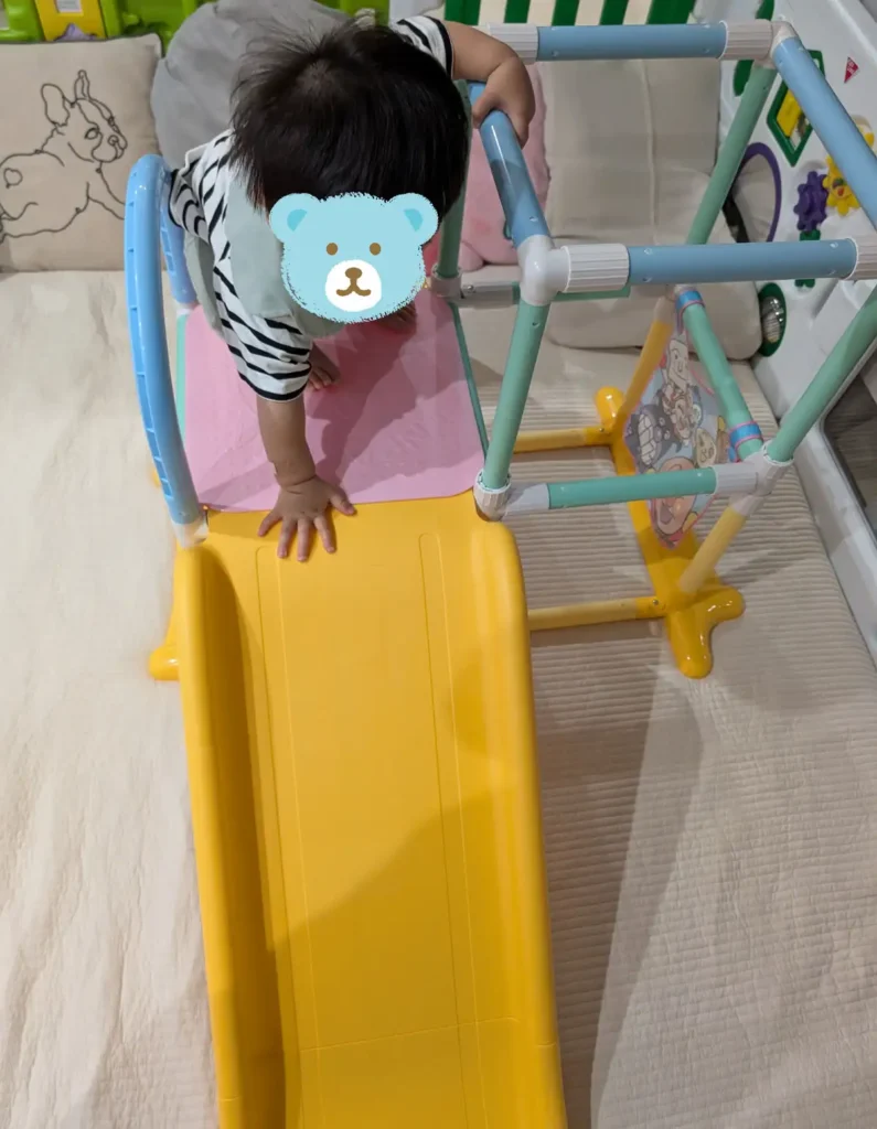 室内ジャングルジムで滑り台を使って遊ぶ1歳児の様子
